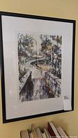 Framed limited edition art print depicting a scenic pathway with trees and lamp posts, black frame and white mat, displayed against a wall with books below.