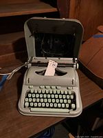 Front view of Hermes 3000 manual typewriter inside its open carrying case on a wooden surface.