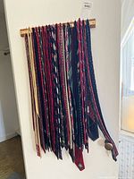 30-40 assorted men's neckties hanging on a rack, showing variety in colors and patterns including stripes, paisley, and solids.