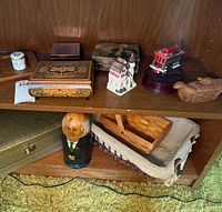 Shelf with various decorative boxes, ceramic figurine, matryoshka doll, woven basket, and tram model arranged on two levels