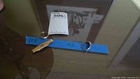 Three pieces on table labeled with blue tape “14K” and “10K” (tie bar, wedding band, class ring)