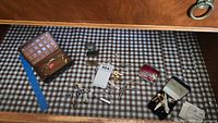 Wide view of assortment of men's vintage accessories including multiple cufflinks, tie bars, tie tacks, pins, and money clips displayed on a checked fabric surface alongside several vintage cases.