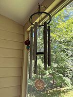 Full view of the metal and wood wind chime hanging outdoors showing five metal chimes, round metal ring top, and decorative elements including beads and wooden ball.