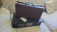 Onkyo TA-R22 stereo cassette tape deck on light couch with brown carrying case on top.