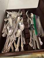 Assorted silverplate flatware pieces including forks, spoons and cutting utensils with ornate floral handles laid in a storage tray
