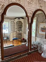 Pair of large wooden framed wall mirrors with arched tops and beveled edges, reflecting a room interior