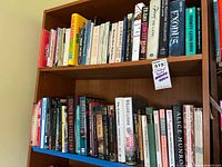 Shelf with approx. 30-40 assorted hardcover and paperback novels and literature books organized side by side with titles visible.
