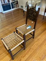 Full view of the carved wood chair with woven seat and matching ottoman side by side on wood floor.