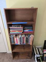 Front view of the five shelf solid wood bookcase showing contents on two middle shelves and visible wood grain.