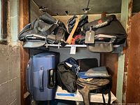 Wide view showing several soft bags including duffel bags, rolling suitcase, and backpacks in black, blue, and red colors.