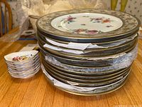 Stack of 11 large dinner plates with gold rim and small stack of 8 serving dishes visible at side