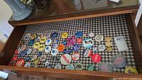 Wide view of a display drawer showing multiple vintage pinback buttons and badges placed on black and white checkered fabric