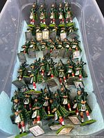 Overview of bin with roughly 40 green-uniformed bagpiper toy soldiers, some standing, some lying