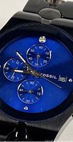 Close-up of dial showing blue face, subdials, logo, and crystal accent