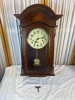 Front view of wood wall pendulum clock with key shown