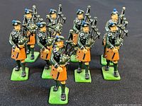 Group view of ten painted metal Irish Guards piper figurines on green bases