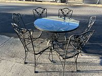 Full view of round glass-top table with six metal chairs