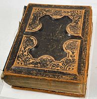 Full view of the large leather-bound Bible showing worn cover with embossed design and detached front cover.