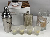 Full view of the cocktail shaker, four frosted lemon motif glasses, hammered hip flask, glass pitcher with label, and boxed Marcellin cocktail smoking and infusion kit.