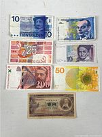 Top view of 7 different foreign banknotes laid out on a white surface, showing clear details of images and text from Netherlands, Germany, France and Japan.