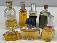 Seven vintage cologne and perfume bottles arranged on a white table, showing various styles, colors, and cap types.