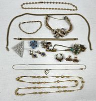 Full overview of costume jewelry lot showing various necklaces, bracelets, rings, pins and earrings laid out flat on white fabric