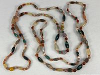 Full view of two long stone and mineral bead necklaces laid out on white background, displaying strand length and mixed bead shapes and colors.