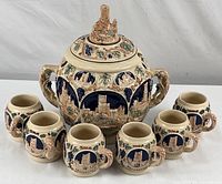 Full view of punch bowl with 7 matching mugs arranged around it, showing overall set and embossed castle scenes.