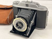Camera front with bellows extended and canvas pouch in background.