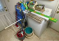Overall lot showing vacuum, ladder, drying rack, mop set, buckets, basket, cleaning supplies, light bulbs, boxed blinds