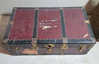 Closed trunk showing red panels, black metal bands, brass hardware and travel decal