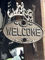 Oval cast-iron plaque side showing "WELCOME" text on scroll bracket