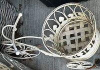 Top view of white metal rolling planter stand showing scrollwork, shells, wheels, basket