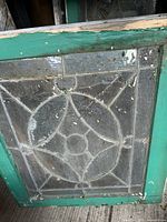 Front view of one panel showing geometric leaded glass pattern and green-painted wood frame
