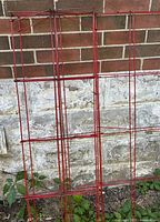 Red steel lattice plant trellises leaning against brick wall