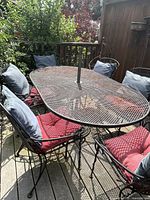 Full view of oval metal mesh table, six metal chairs with cushions around it, umbrella hole visible