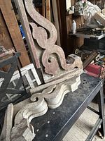Front angled view of both carved wood corbels showing scrollwork and paint wear