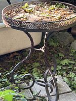 Full view of wrought iron accent table showing round top, twisted legs, scroll feet, rust patina