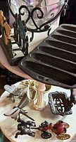 Overview of lot showing glass bowl in scroll cradle, picket fence floral figure, cornbread pan, insect trivets, brass scoop, openwork trivet and cast iron toy pieces