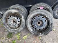 Four steel rims with mounted tires leaning against vehicle