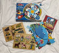 All five puzzles grouped: boxed circular floor puzzle, Wonder Woman boxed puzzle, two wooden peg puzzles, loose foam puzzle pieces