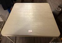 Top view of square beige folding card table showing surface texture and dip