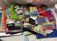 Pile of assorted office supplies including binders, stapler, marker packs, clips, memo pad