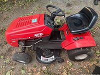 Left side view of red MTD riding lawnmower tractor showing seat, steering wheel and mower deck