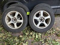 Two tires on alloy rims leaning against vehicle