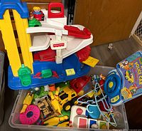 Fisher-Price parking garage ramp atop bin with assorted toys visible