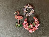 All three brooches laid out: flamingo, wreath, floral spray