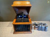Phonograph open with cylinders beside cabinet