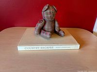 Plaid fabric bear seated on top of Country Escapes hardcover book showing spine title