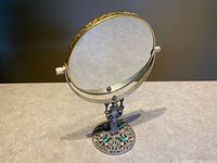 Front view of gilt round swivel mirror on filigree base with turquoise cabochons